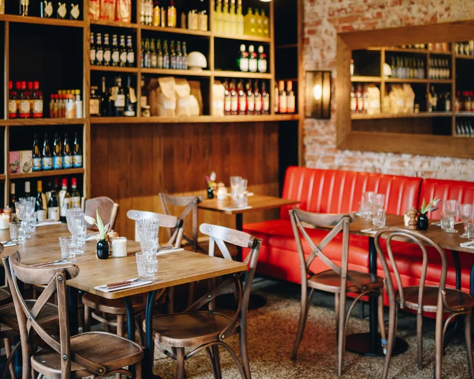 Pizzeria Luca: Restaurantområde med træborde, røde bænke og flaskereoler.