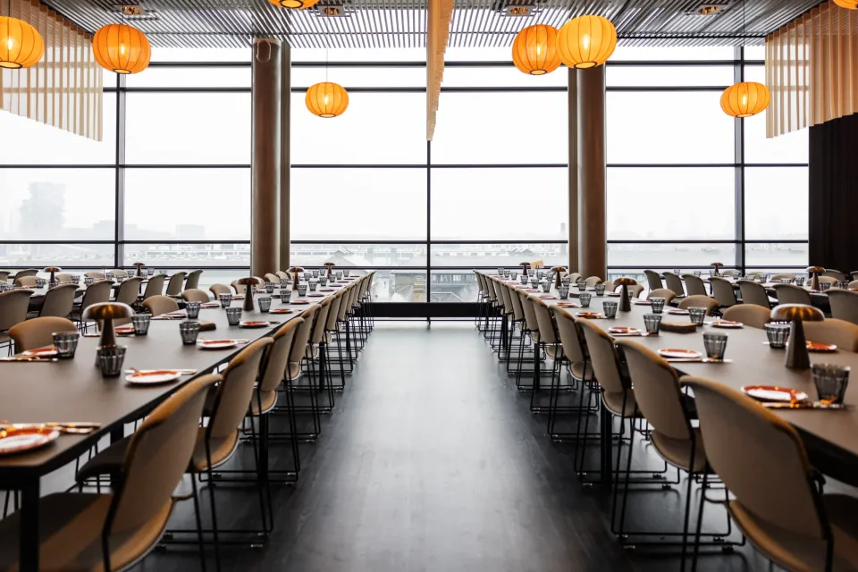 CPH Conference - en del af DGI Byen: Lange dækkede borde ved en høj glasfacade med runde orange pendler.