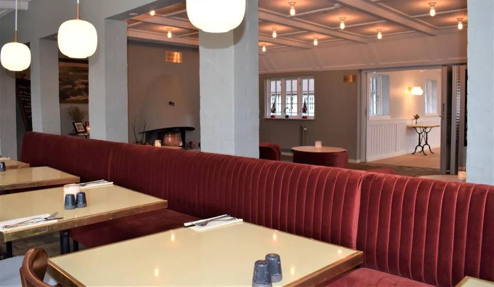 Selskabslokalet v. Hotel Nørrevang: Restaurantborde langs en rød polstret vægbænk mellem lyse søjler.