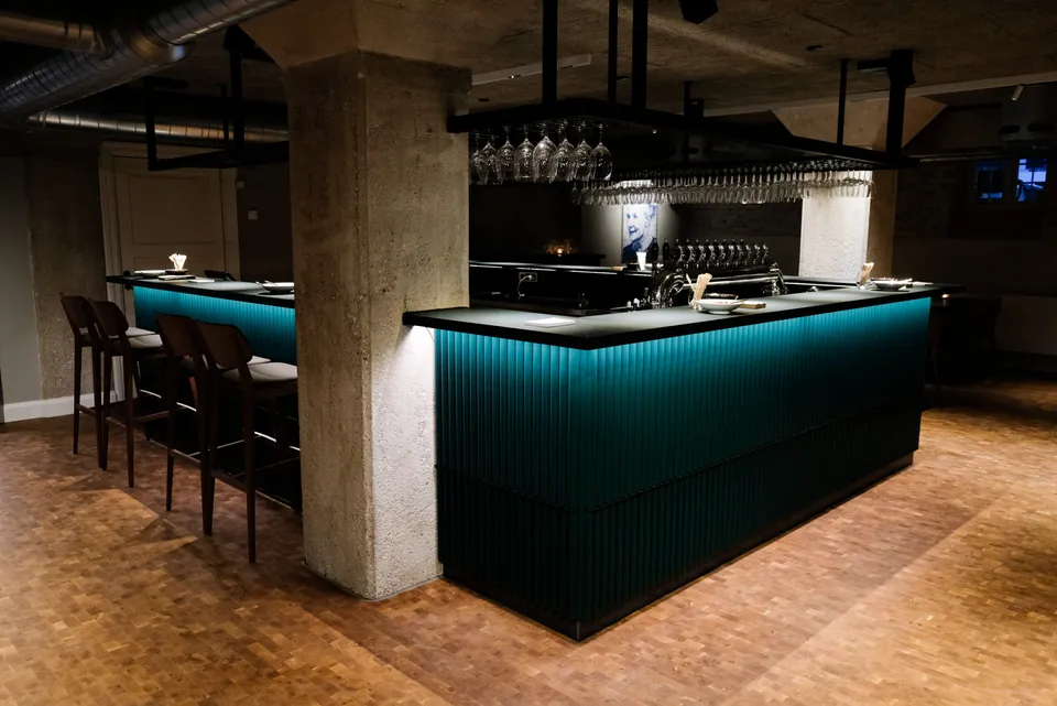 Nobel Bar: Grøn bar omkring en betonsøjle med høje stole og hængende glas.