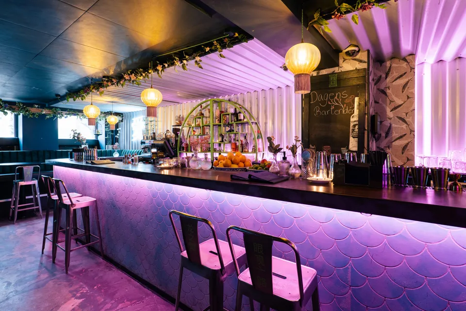 Little Green Door: lang bar med høje stole og lilla belysning.