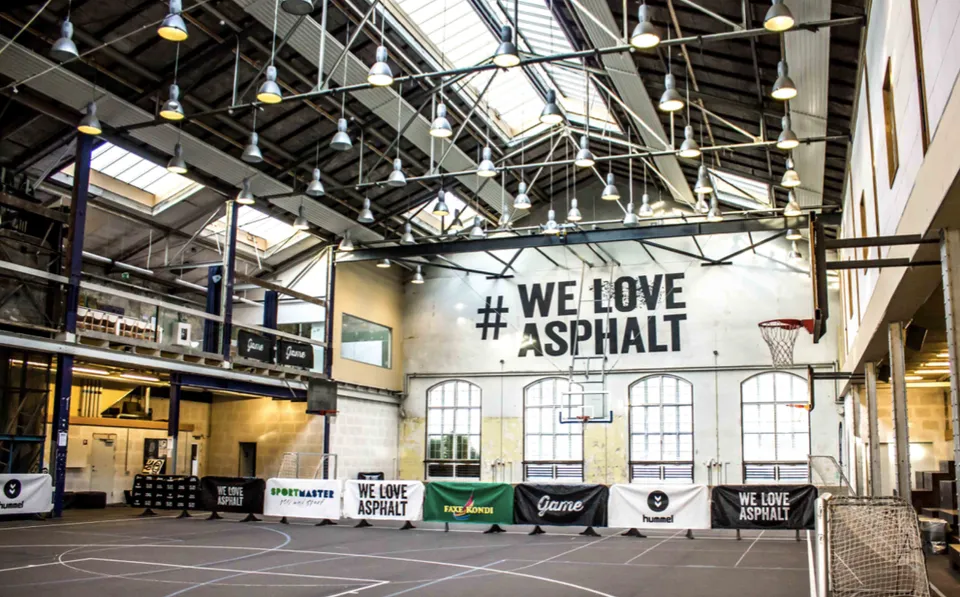 Store Hall v. Game Streetmekka: Stor idrætshal med basketballbane, høje vinduer og synlige loftsbjælker.