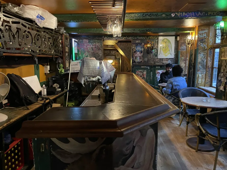 Moose Bar: Bar med mørk disk, små borde og vægge dækket af tegninger og skrift.