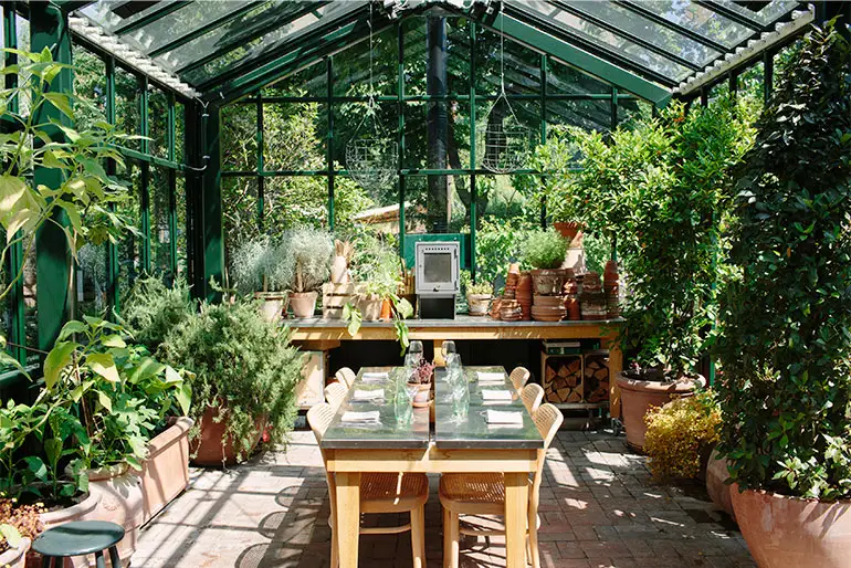 Drivhus & Køkkenhave v. Restaurant Kilden: Drivhus med glasloft, grønne planter og et langt dækket bord.
