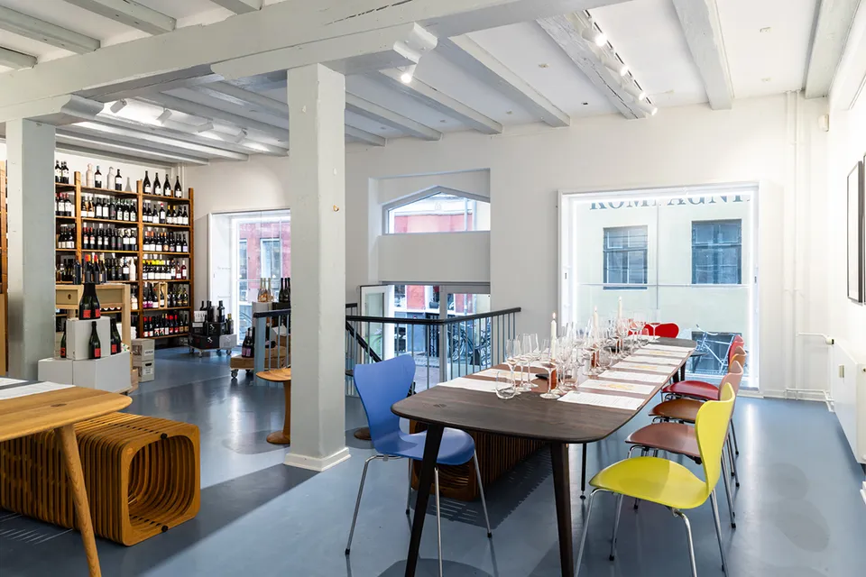 The Great Wine Experience: lyst vinlokale med dækket langbord, farvede stole og store vinreoler.