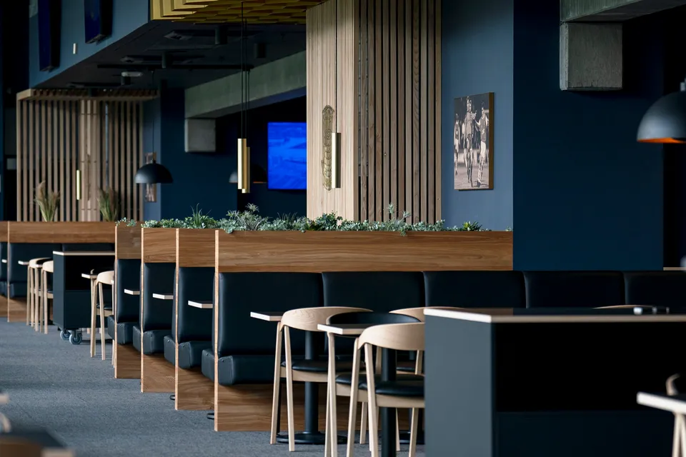 Vilfort Lounge v. Brøndby Stadion: Lounge med borde, høje stole og træbeklædte søjler.