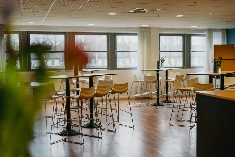 Business Club Lounge v. Parken: høje borde og stole i et lyst loungeområde med store vinduer.