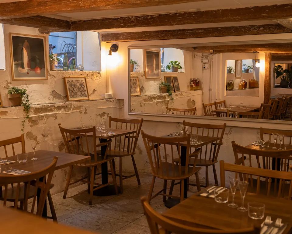 Norrlyst: træborde og stole i et varmt belyst restaurantlokale med spejl og loftsbjælker.