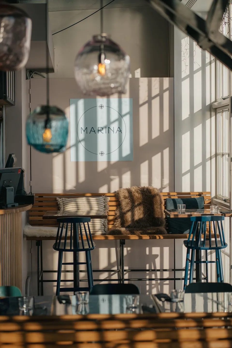 Seaside Toldboden: høje borde og stole foran store vinduer i et restaurantområde.