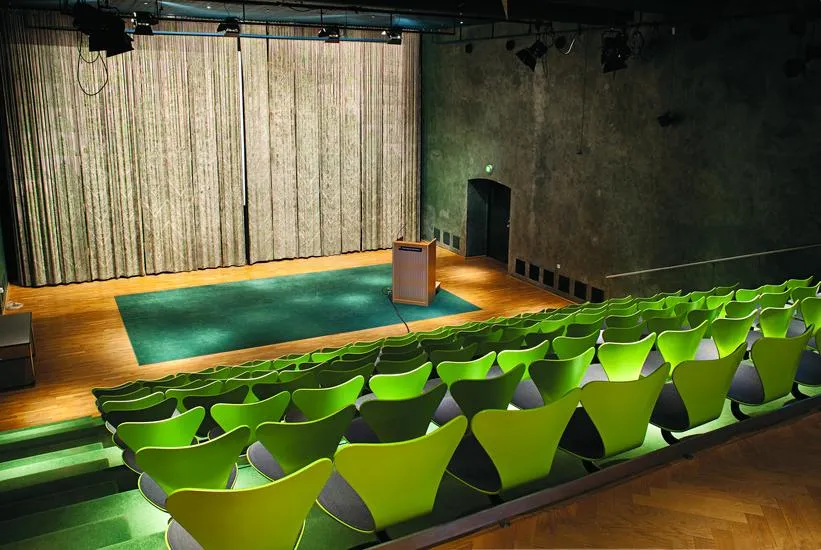 Biografteatret v. Nationalmuseet: Grønne sæderækker foran en scene med gardin og talerstol.