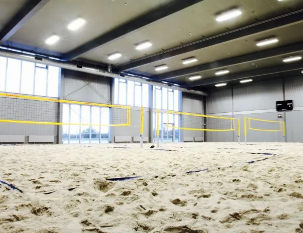 Beachvolleybanerne v. Hafnia Hallen: Indendørs sandbane med volleyballnet, store vinduer og loftslamper.