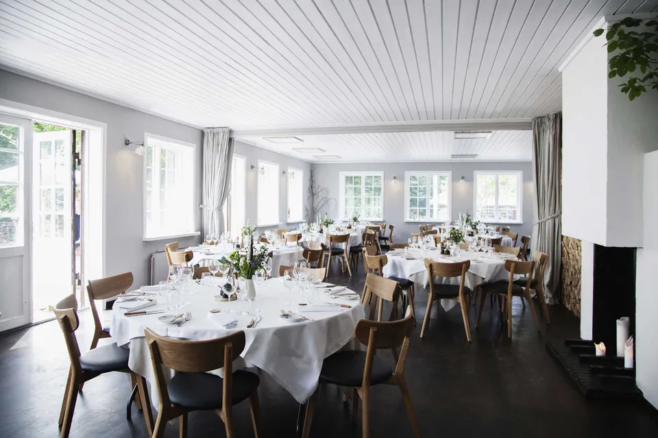 Hovedhuset v. Herthadalen: Lyst spiseområde med dækkede borde, mange vinduer og en pejs.