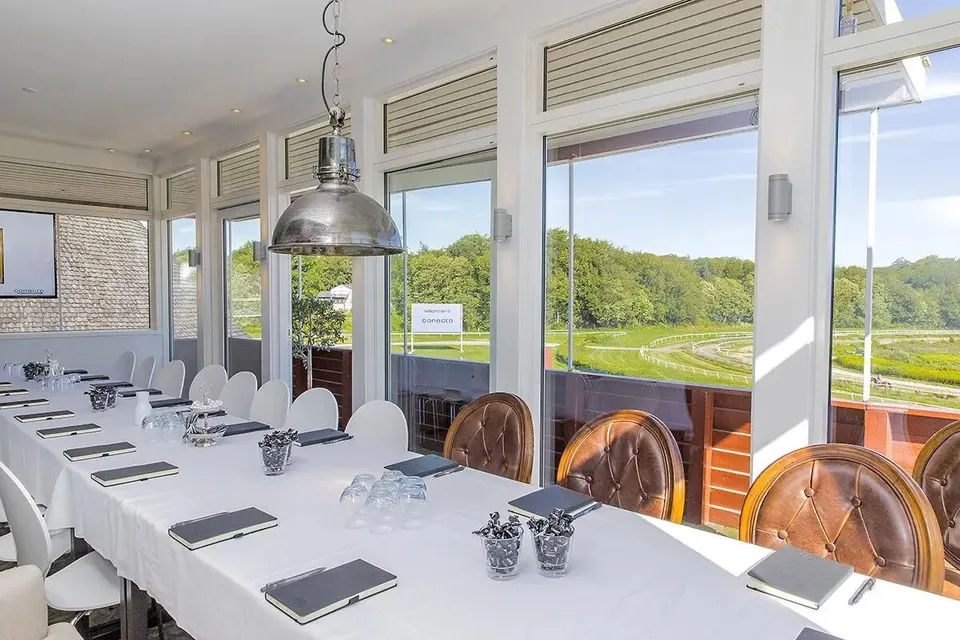 VIP Loungen v. Klampenborg Galopbane: Langt bord med hvide duge foran store vinduer med udsigt til banen.