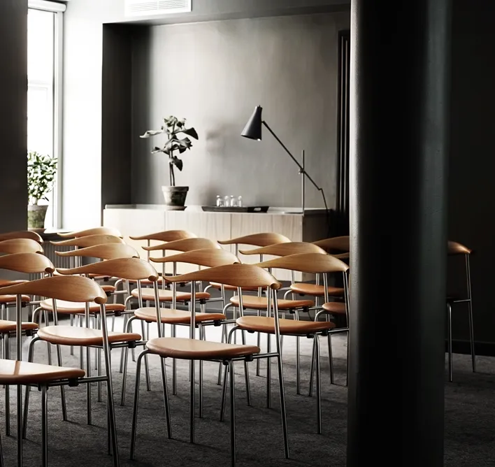 Hotel SP34: Træstole og borde i et mørkt hotelrum med lyse vinduer.