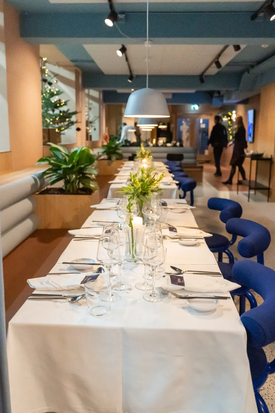 Workbar Restaurant v. Matrikel1: Workbar Restaurants lange dækkede bord mellem siddeområder og planter.