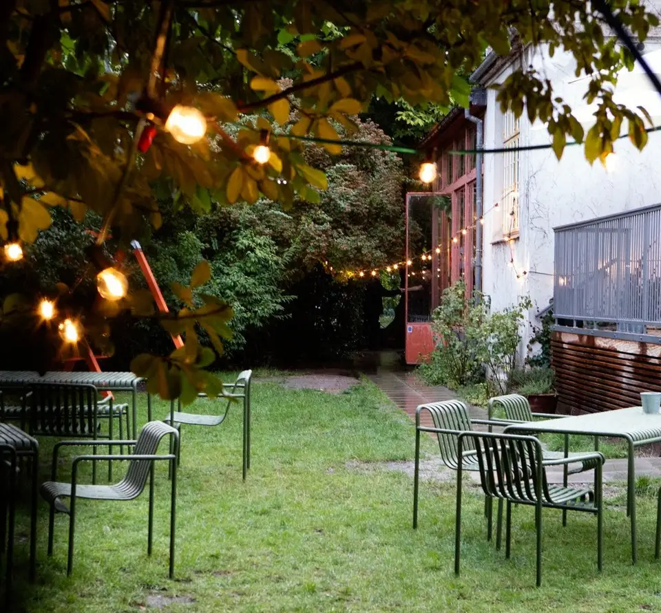 Haven & Baggården v. Villa Kultur: Caféborde og stole på en græsplæne under træer og lyskæder.