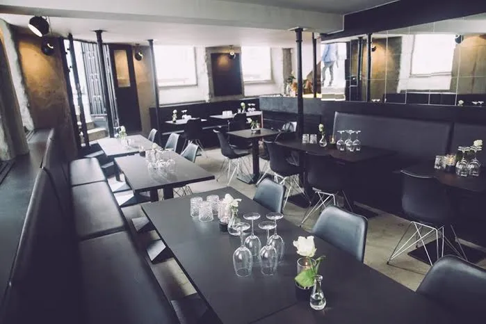 Restauranten v. KöD København: Restaurantområde med sorte borde, mørke bænke og store spejle.