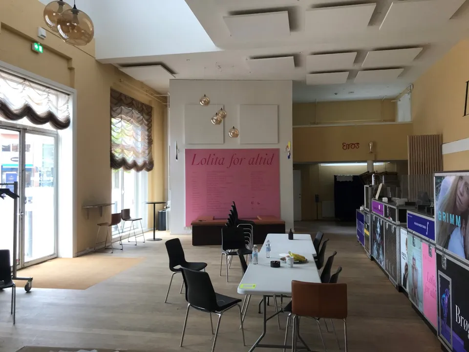 Revolver Foyer v. Teater Republique: Borde og stole i en lys foyer med store vinduer og en lang skranke.