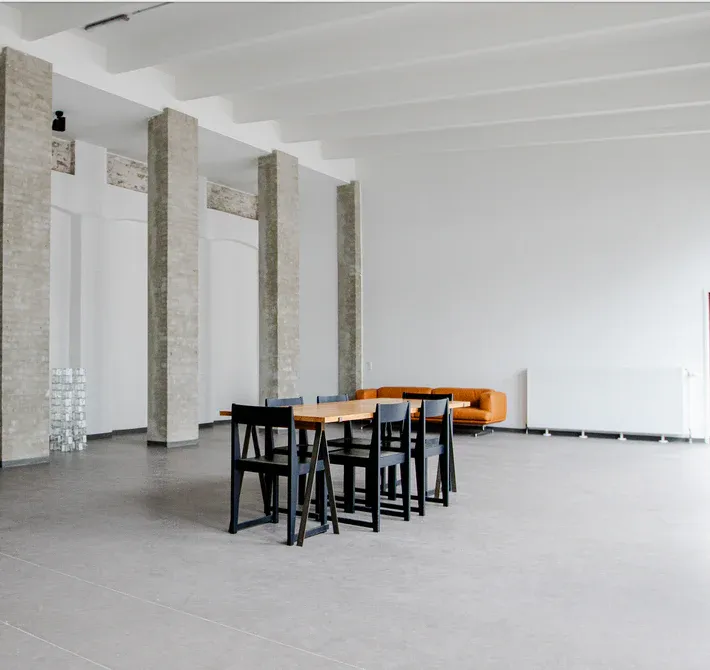Aeris Studio: lyst studiorum med synlige søjler, et højt bord og sorte stole.