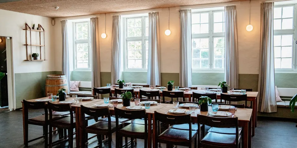Brede Høker: Restaurantborde og mørke træstole foran en række lyse sprossevinduer.