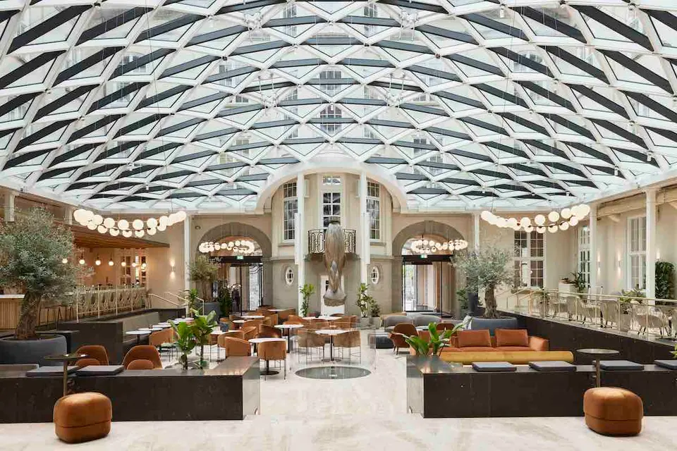 Courtyard Bar v. Villa Copenhagen: Stort lyst atrium med buet glasloft, planter og loungemøbler.