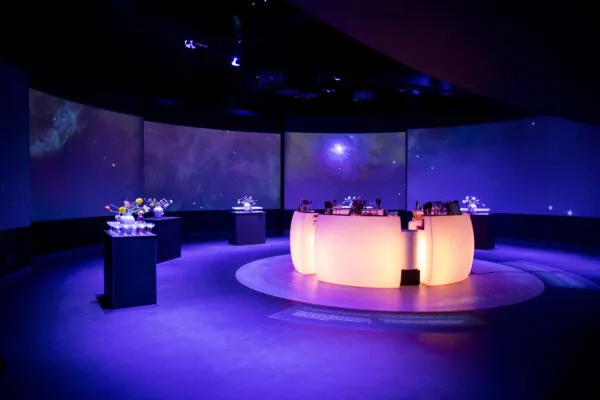 Kosmos v. Planetarium: rund lysende bar i et mørkt rum med farvede projektioner.