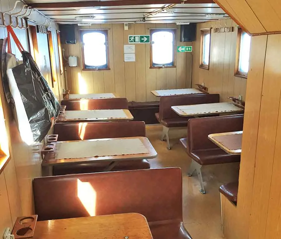 M/S Øby v. Spar Shipping: Træbeklædt skibssalon med bænke, små borde og vinduer.