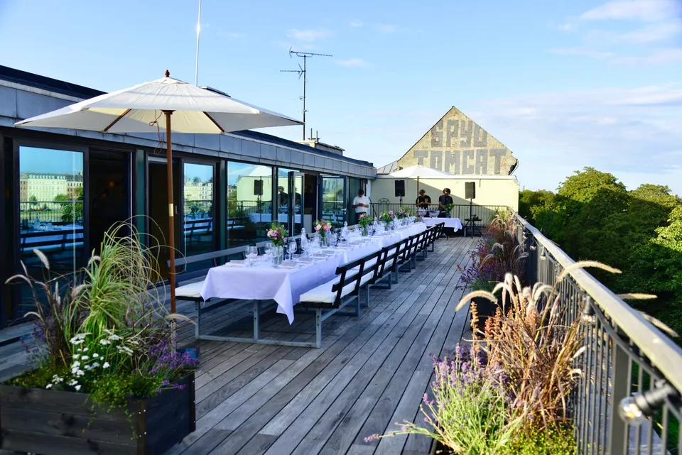 Terrassen: Træterrasse med et langt dækket bord langs en glasfacade.