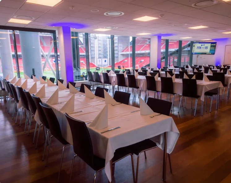 Ambassador Club Lounge v. Parken: lange dækkede bordrækker i en lounge med store vinduer og lilla lys ved søjlerne.