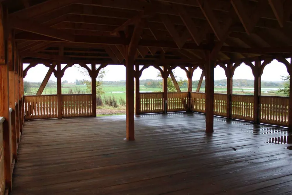Pavillonen v. Ravnsborg: Åben træpavillon med stolper, trægulv og udsyn til grønne omgivelser.