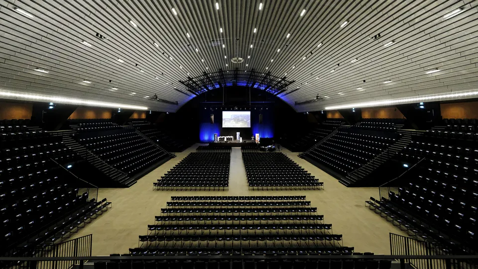 KB Hallen: Stor sal med stolerækker, tribuner og en scene for enden.