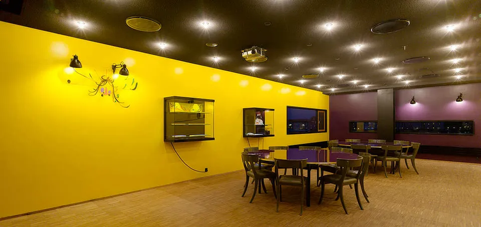 Kørner Lounge v. Skuespilhuset: Lounge med gule og lilla vægge, mørke stole og borde under loftspots.