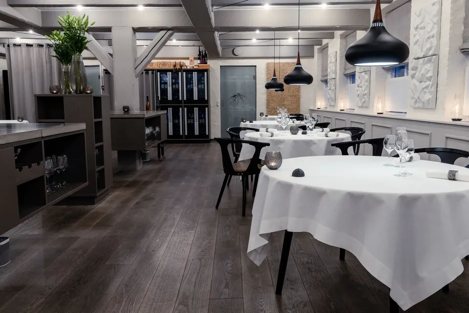 Restaurant Jordnær: Restaurantlokale med runde dækkede borde, sorte stole og store mørke lamper.