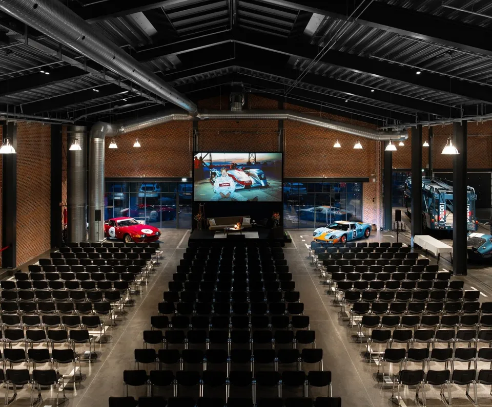 Bilhotellet v. Classic Car House: Det store halrum med scene, en bil og rækker af stole.