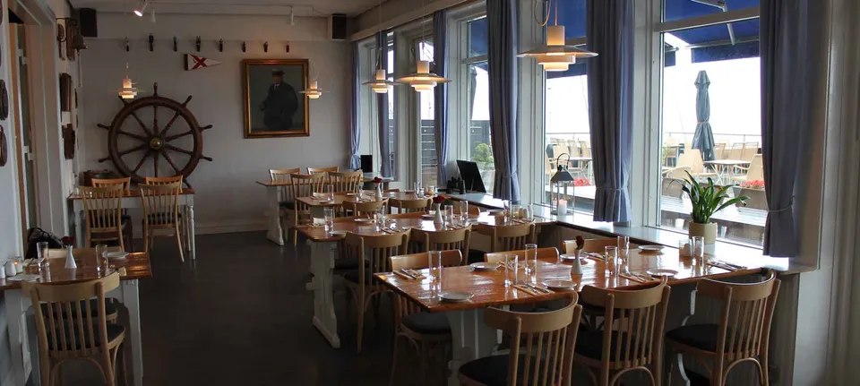 Restauranten v. Hellerup Sejlklub: Dækkede borde ved høje vinduer i et lokale med maritim udsmykning.