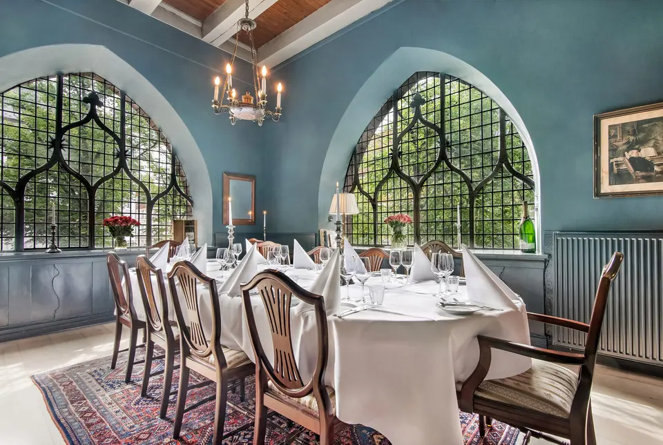 Logestuen v. Restaurant Maven: Dækket bord med træstole i et blåt lokale med store buede vinduer.