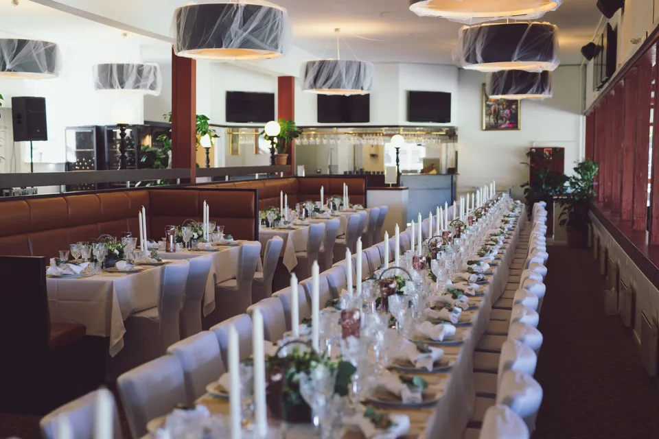 Den Kongelige Restaurant v. Klampenborg Galopbane: Langbord opdækket i en sal med bar, høje vinduer og pendler.