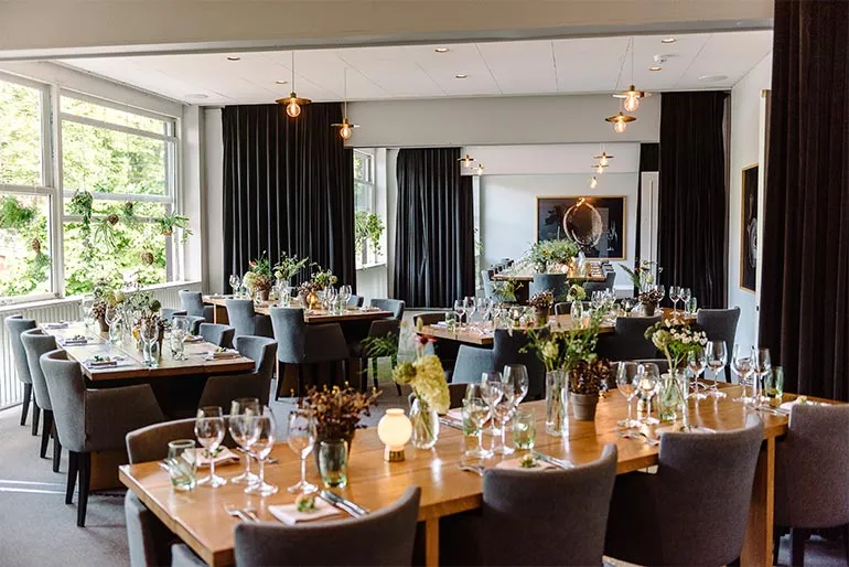Salonerne v. Restaurant Kilden: Spiserummet med dækkede borde, store vinduer og gardiner.