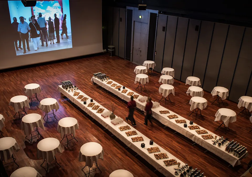 Koncert- og Konferencesalen v. ARKEN: Auditorium med lange serveringsborde og cocktailborde foran en skærm.
