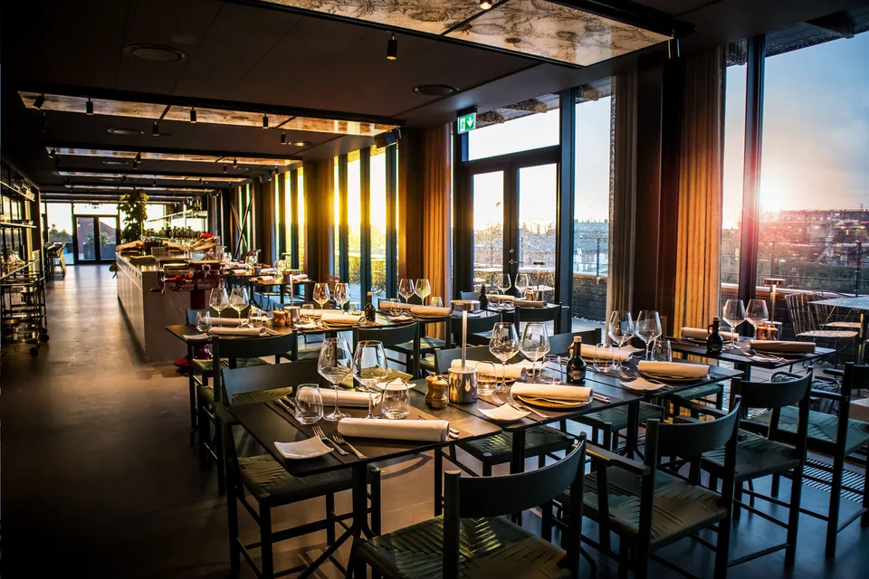 Tramonto Rooftop: Restaurant med dækkede borde og høje vinduer i aftenlys.