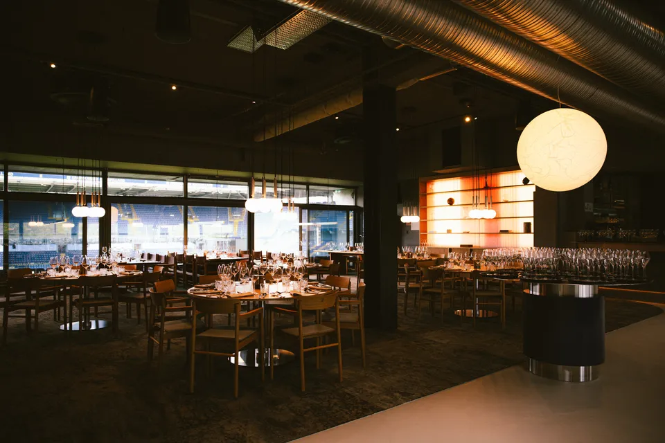 Michael Laudrup Lounge v. Brøndby Stadion: Dækkede borde i en mørk lounge med store vinduer og rund pendel.