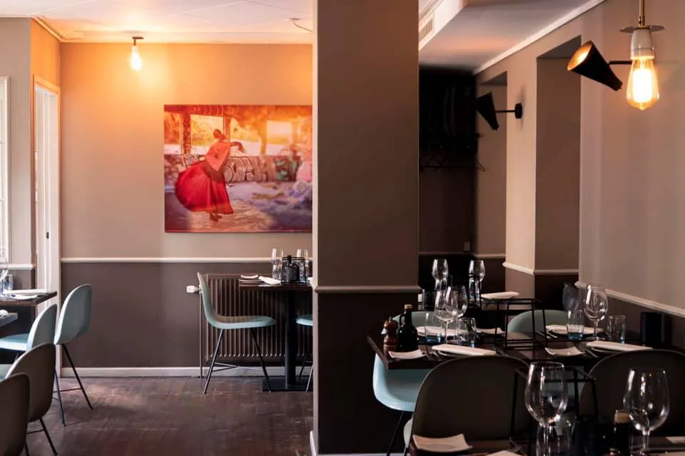 Pintxos: Små dækkede borde og lyse stole i et restaurantområde med vægkunst.