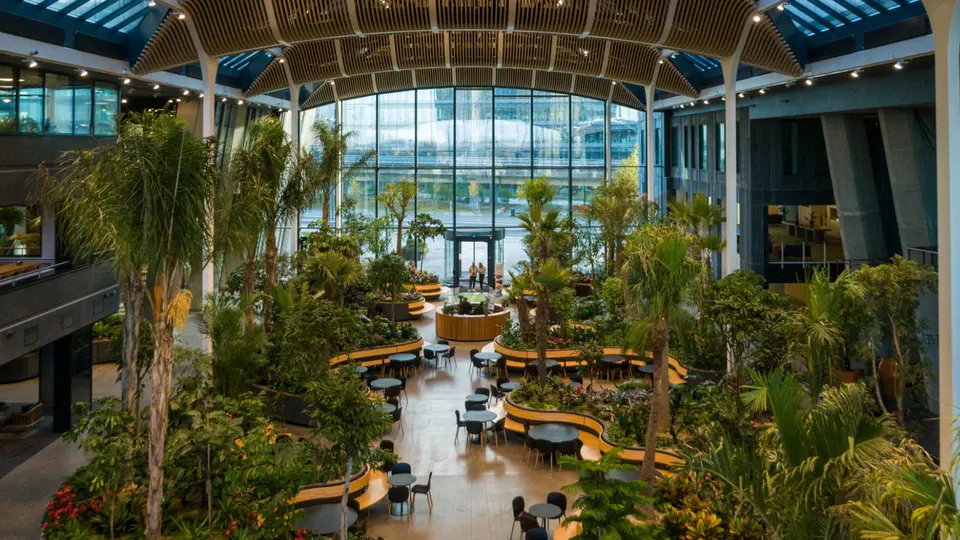 Atrium v. Crowne Plaza Copenhagen Towers: Højt glasoverdækket atrium med mange træer, planter og siddeområder.