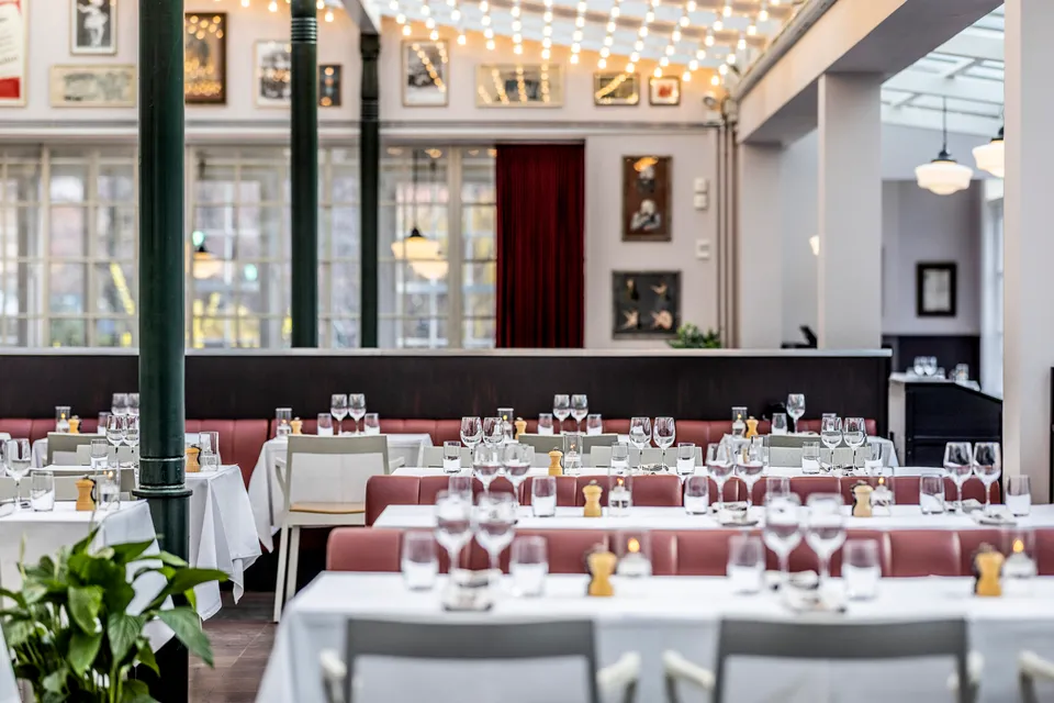 Brdr. Price v. Tivoli: dækkede borde i et lyst restaurantlokale med grønne søjler og billeder på væggene.