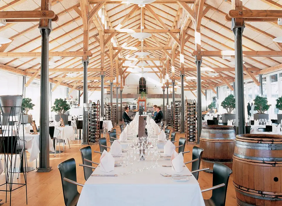 Vestauranten - en del DGI Byen: Dækket langbord under høje træspær mellem mørke søjler.
