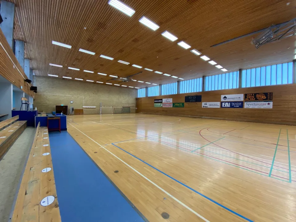 Hal 1 v. Frederiksberghallerne: Sportshal med trægulv, blå gulvfelter og høje vinduer under et træloft.