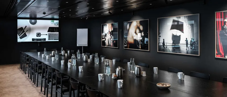 Lounge 2 v. Operaen: Mørk lounge med langt bord, høje stole og store indrammede fotografier.