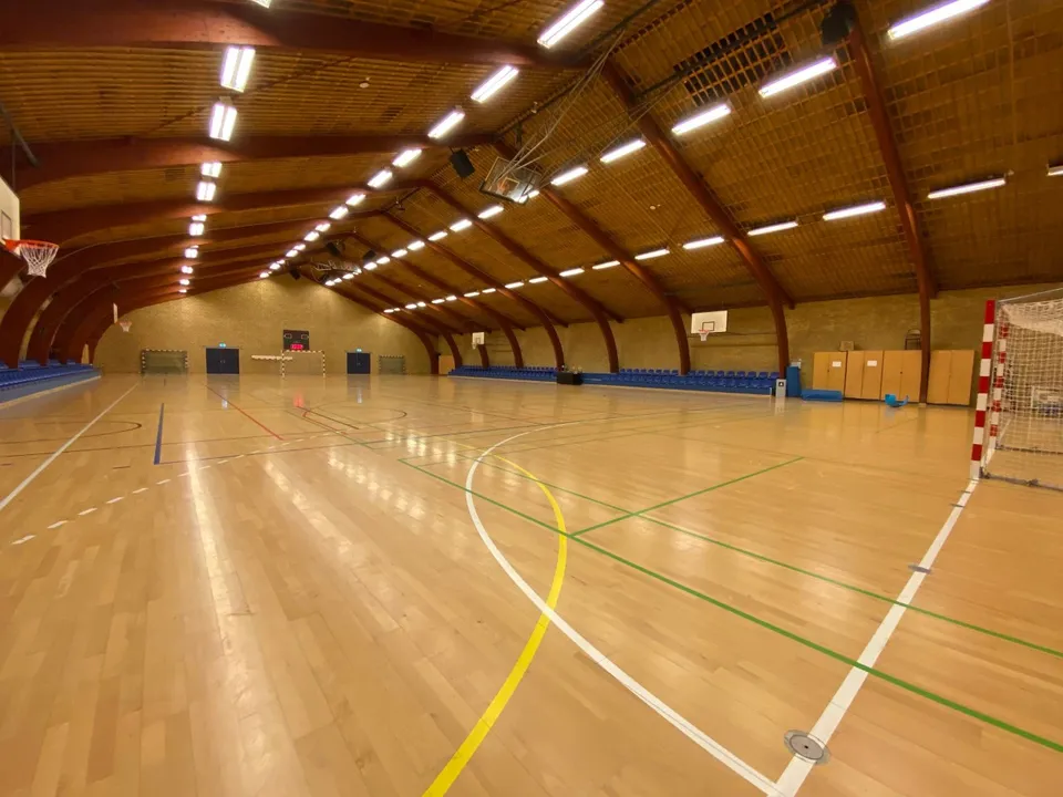 Hal 2 v. Frederiksberghallerne: Stor sportshal med buede træbjælker, trægulv og et håndboldmål.