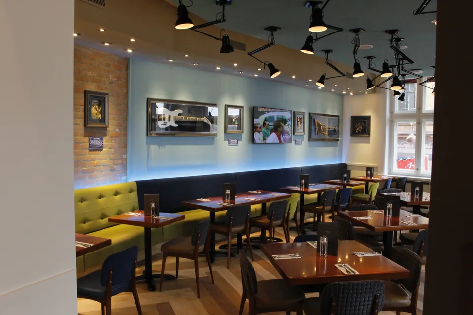Hard Rock Cafe: restaurantborde, stole og en gul bænk under billeder og musikmemorabilia.